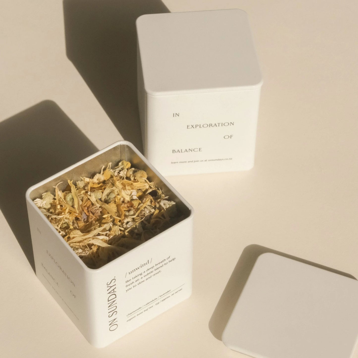 On Sundays Unwind herbal tea in signature white tin with lid, filled with loose organic botanicals including chamomile, calendula, and lavender, shot in soft natural light.