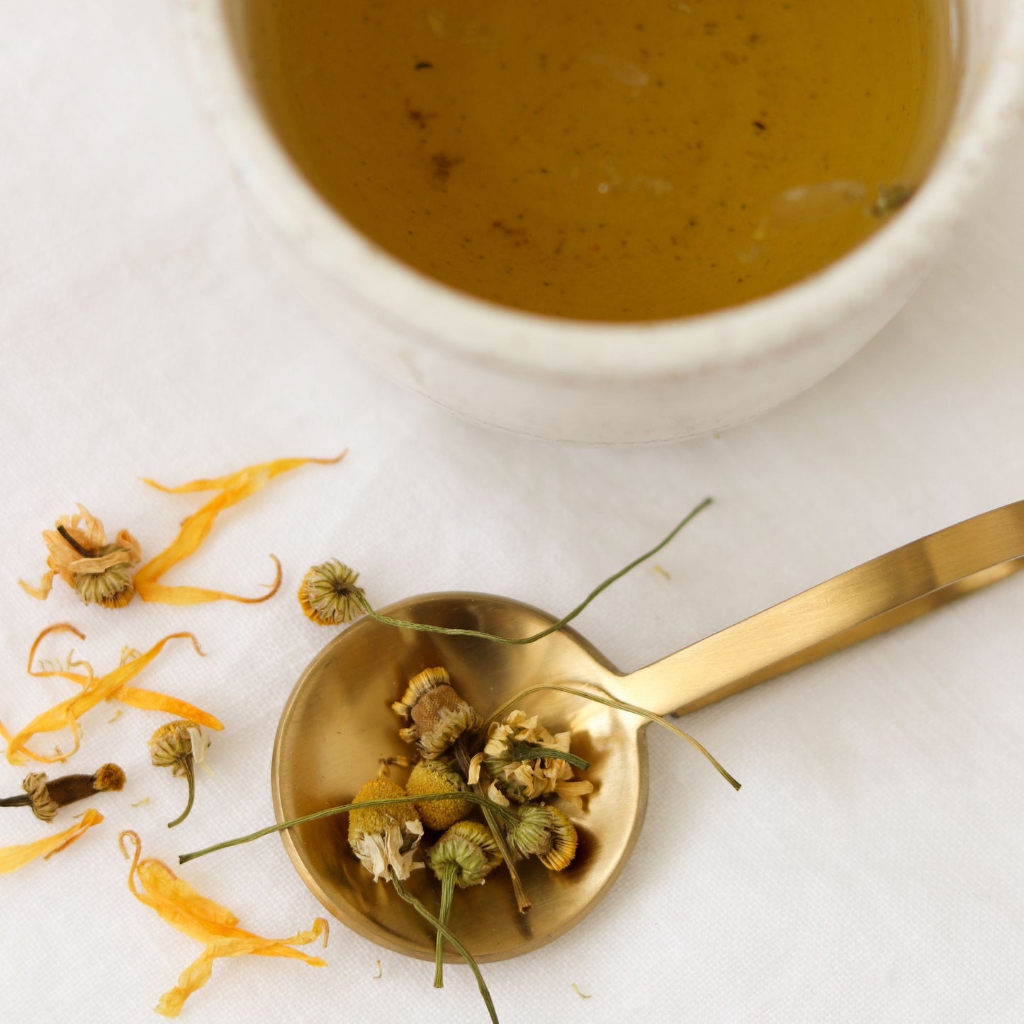 A spoonful of dried chamomile, calendula, and lavender beside a cup of brewed Unwind tea—organic botanicals crafted for a calming bedtime ritual.