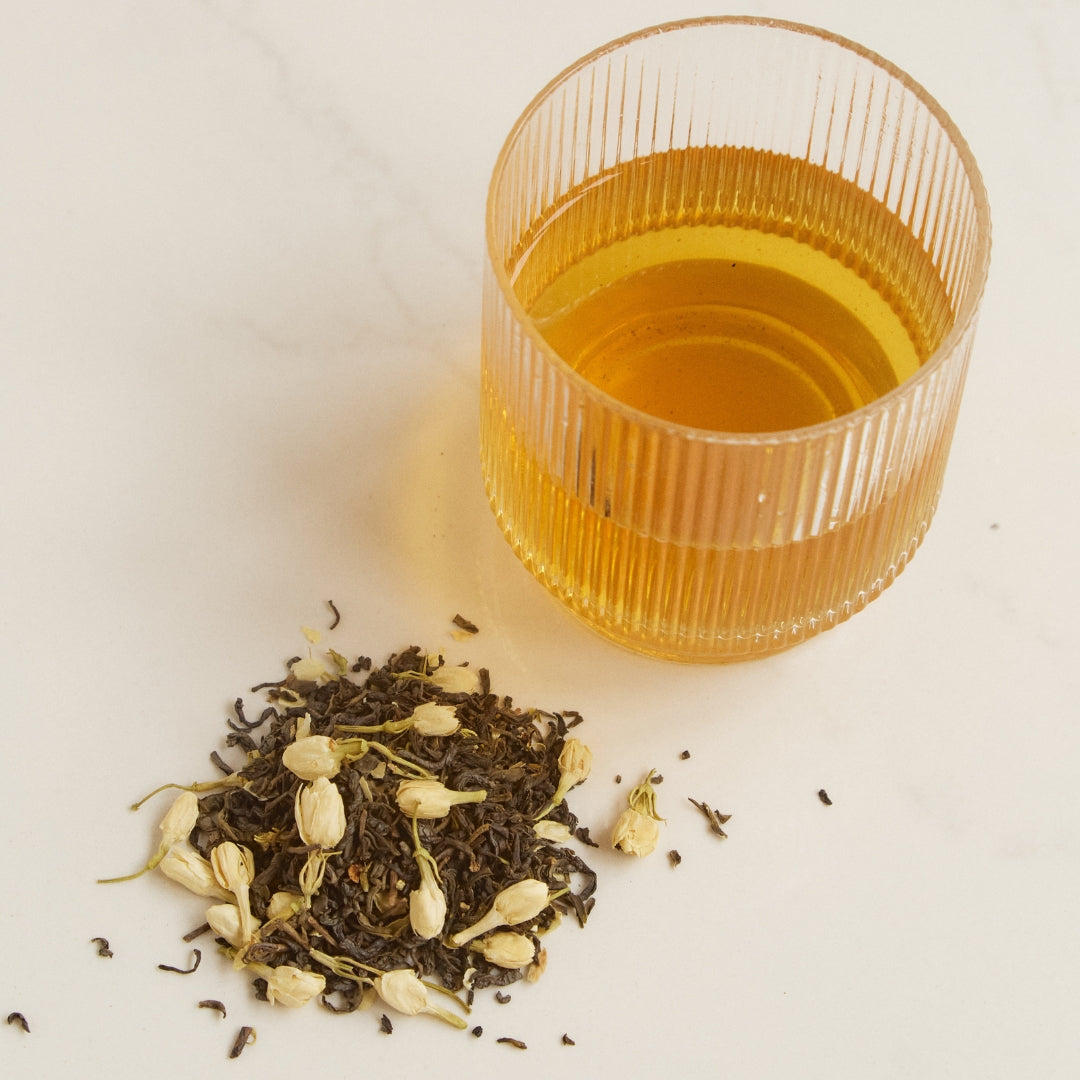 Freshly brewed On Sundays Green Jasmine organic loose leaf green tea in glass with whole green tea leaves and dried jasmine buds.