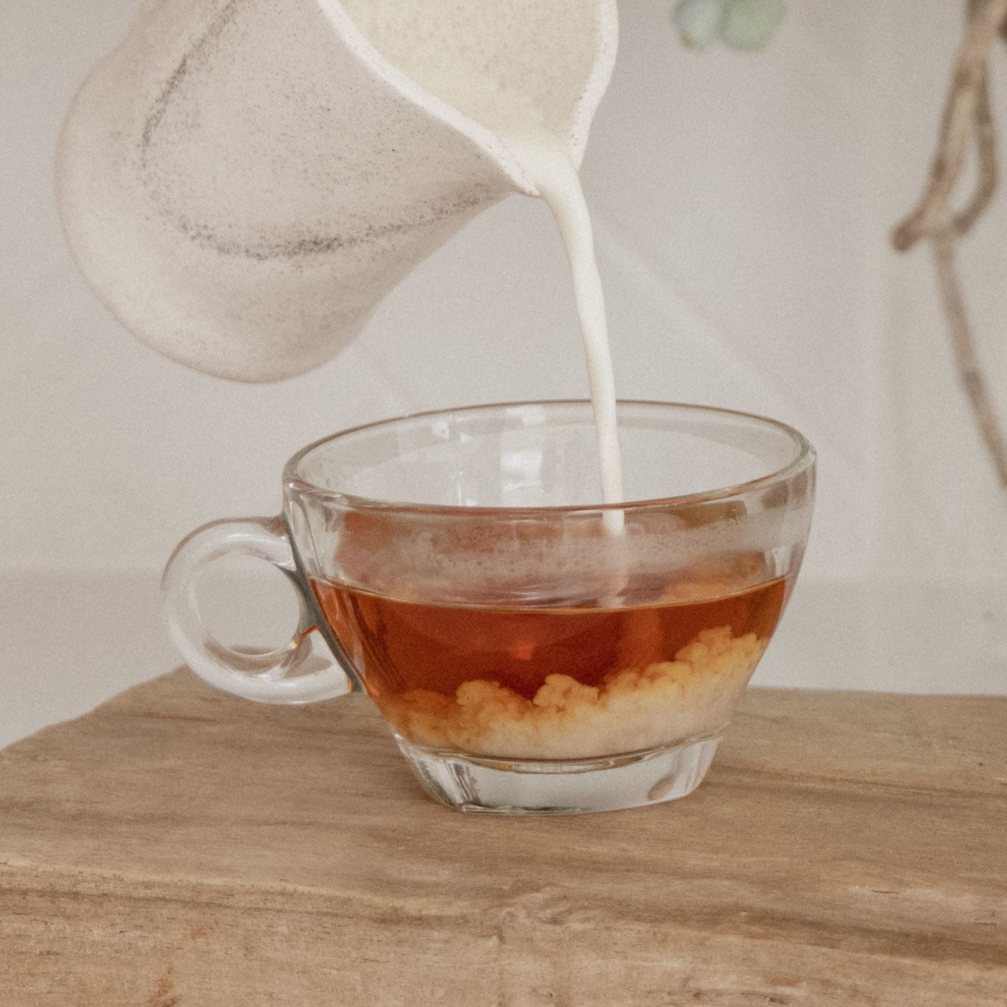 Milk being poured into a glass cup of On Sundays organic English Breakfast tea creating a soft swirling cloud effect.