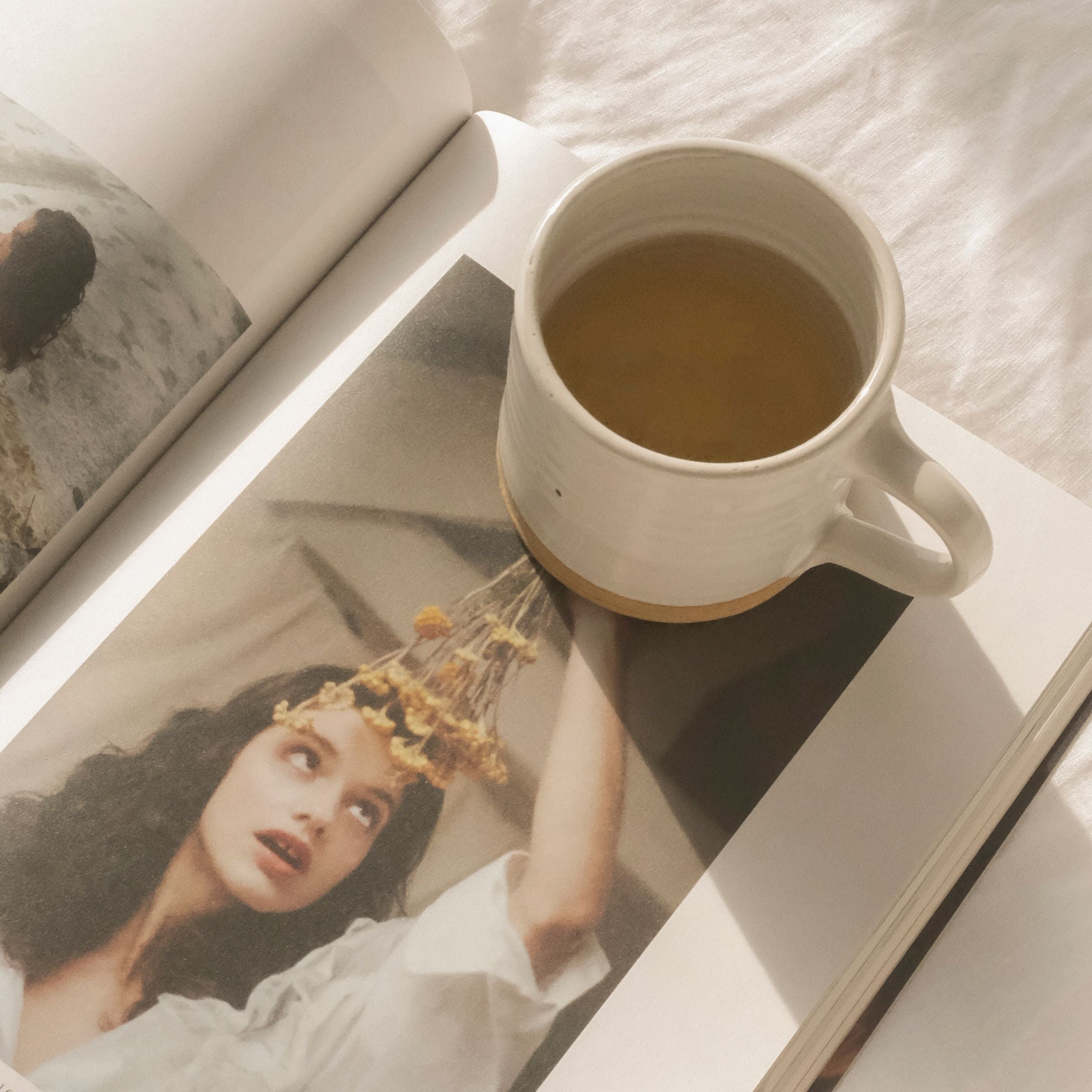 Ceramic cup of On Sundays Mint Tea resting on an open wellness magazine in soft morning light, capturing a calming health and lifestyle moment.