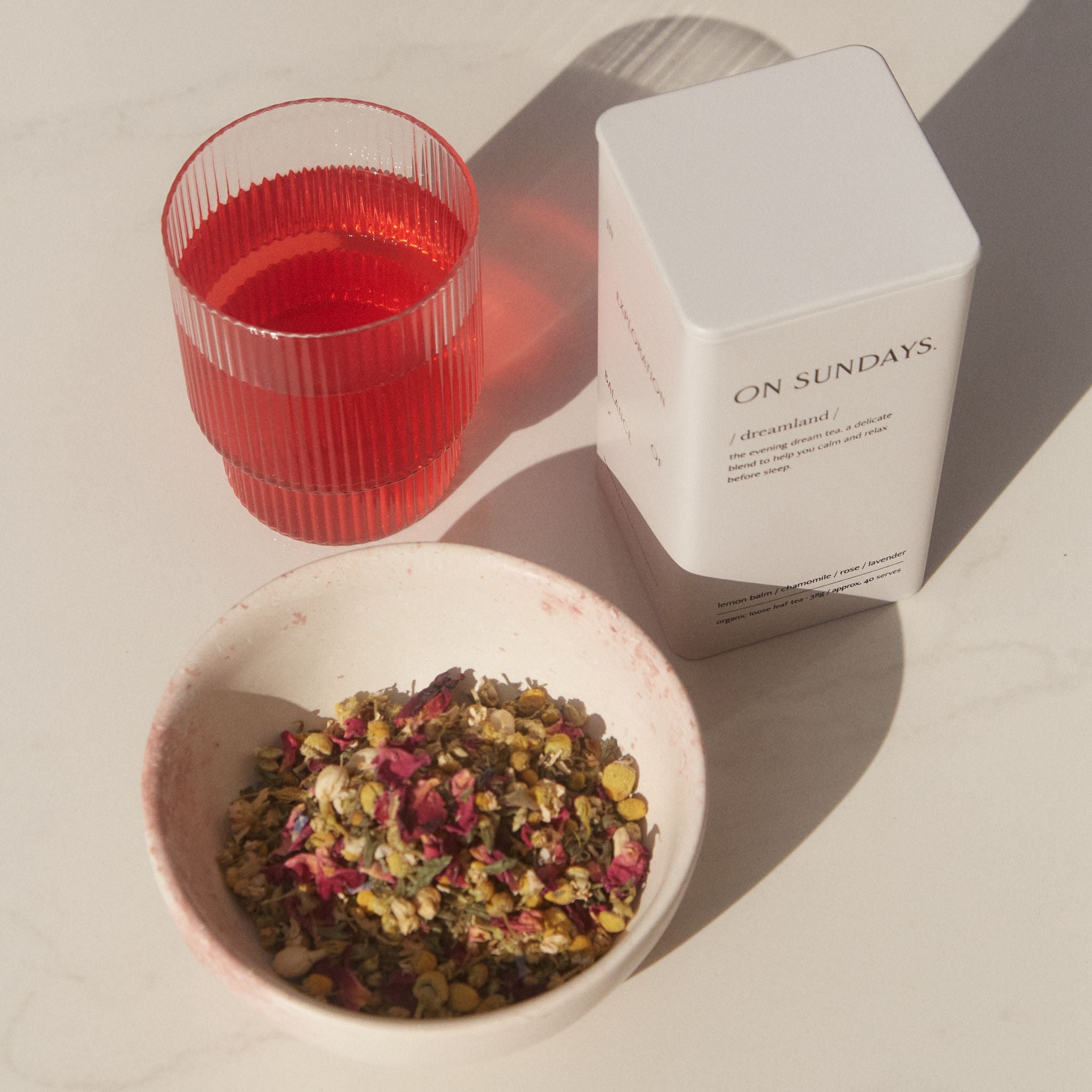 On Sundays Dreamland organic loose leaf sleep tea in white tin with chamomile rose and lavender beside mulled wine herbal tea in glass.