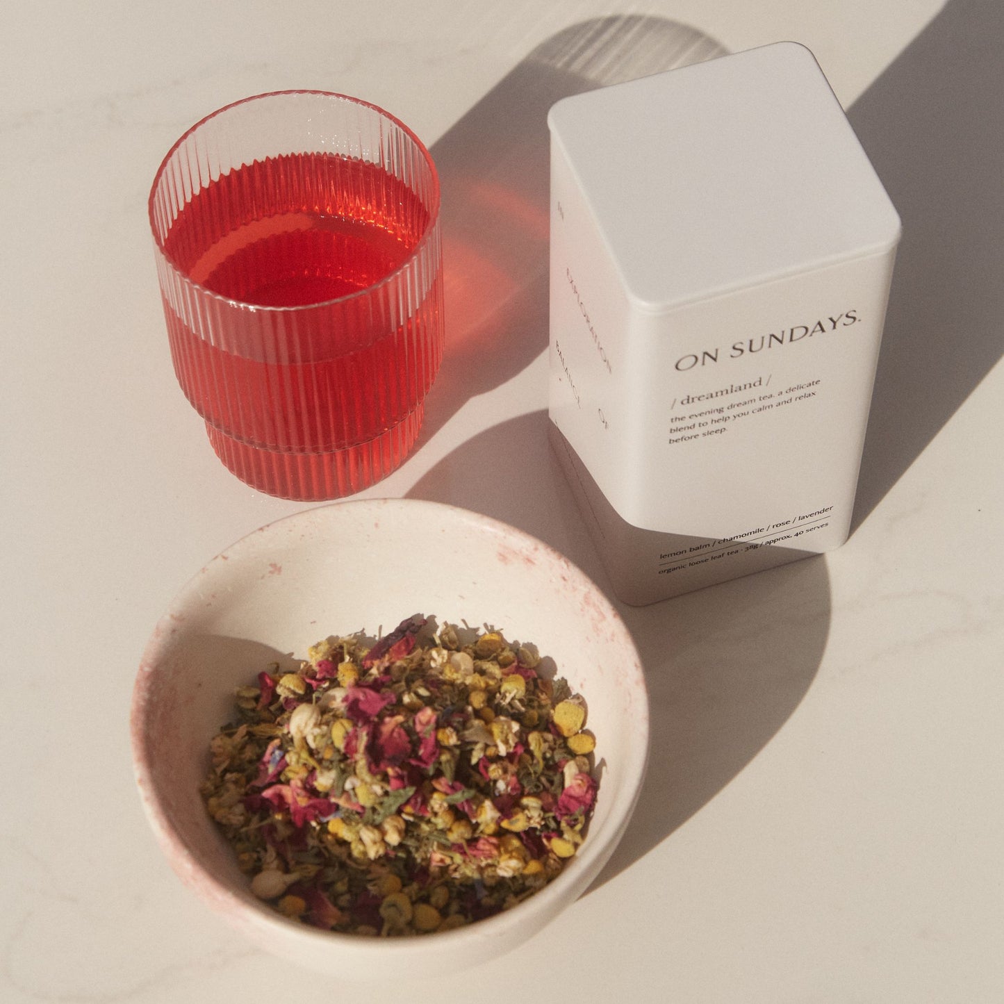 On Sundays Dreamland organic loose leaf sleep tea in white tin with chamomile rose and lavender beside mulled wine herbal tea in glass.