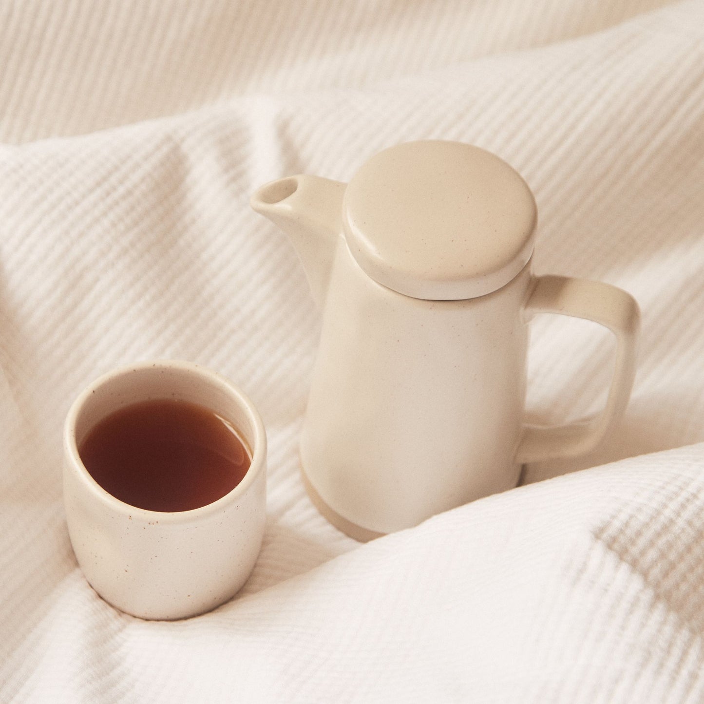 On Sundays English Breakfast tea served in ceramic cup with matching teapot on soft neutral linen.