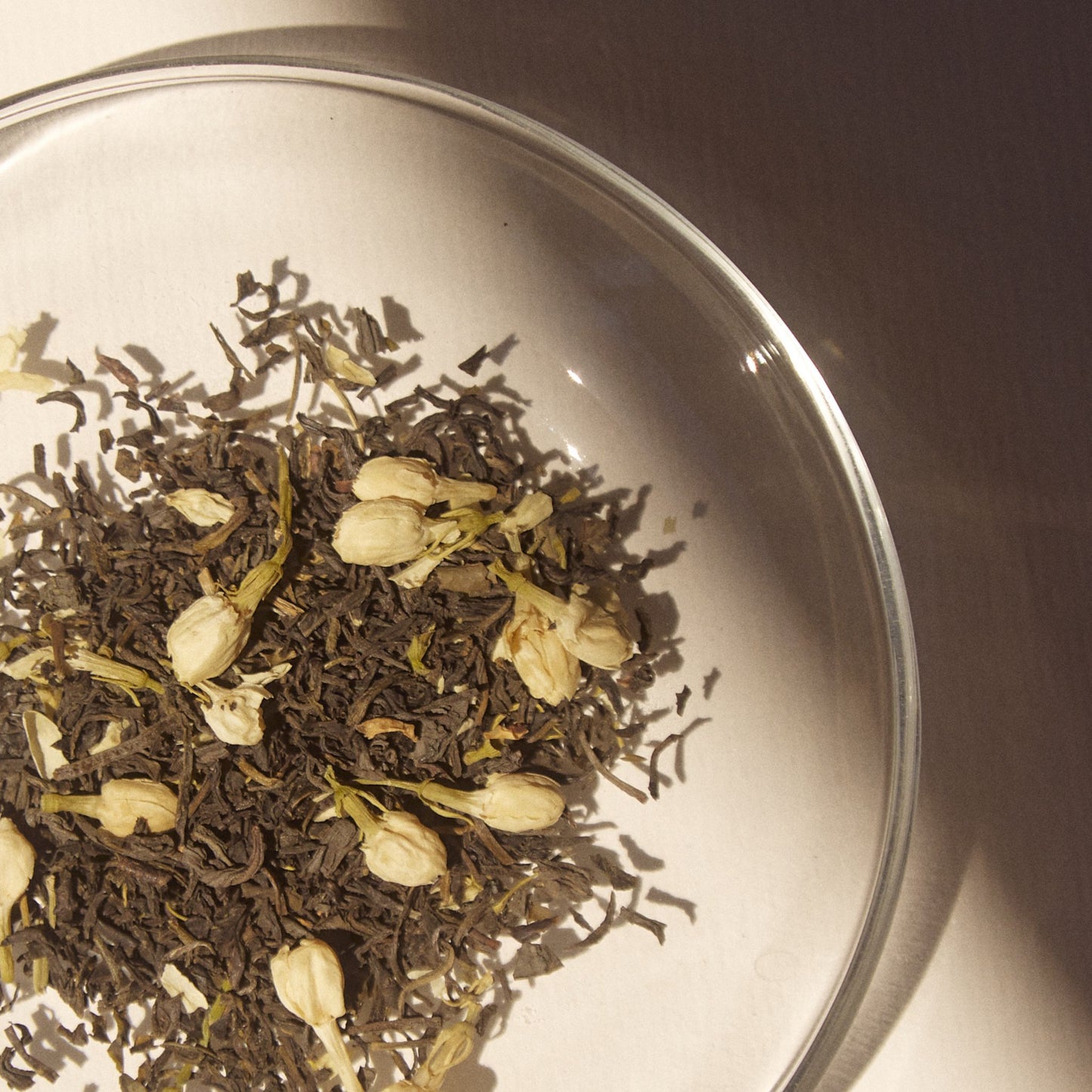 On Sundays Green Jasmine organic loose leaf green tea blend with whole jasmine flower buds and premium green tea leaves in glass dish.