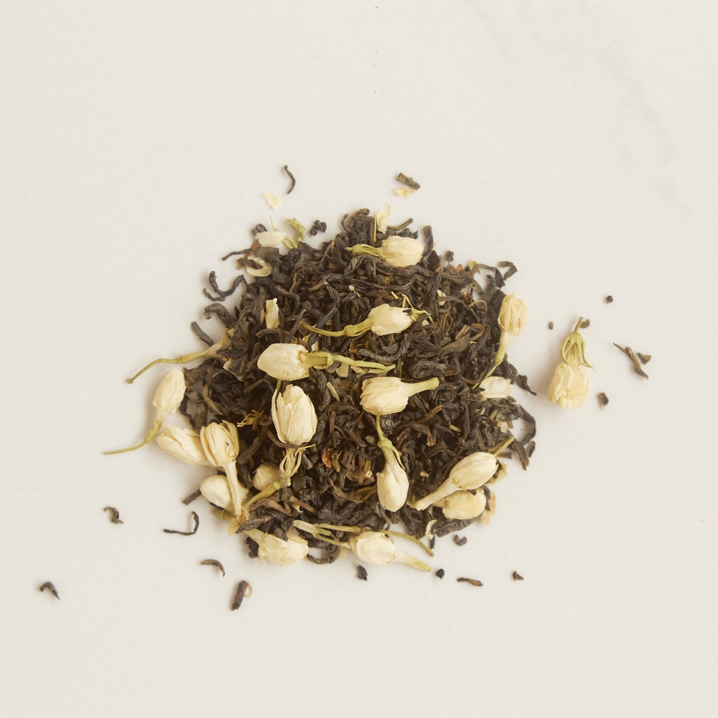 On Sundays Green Jasmine organic loose leaf green tea with whole jasmine flower buds scattered on white surface.