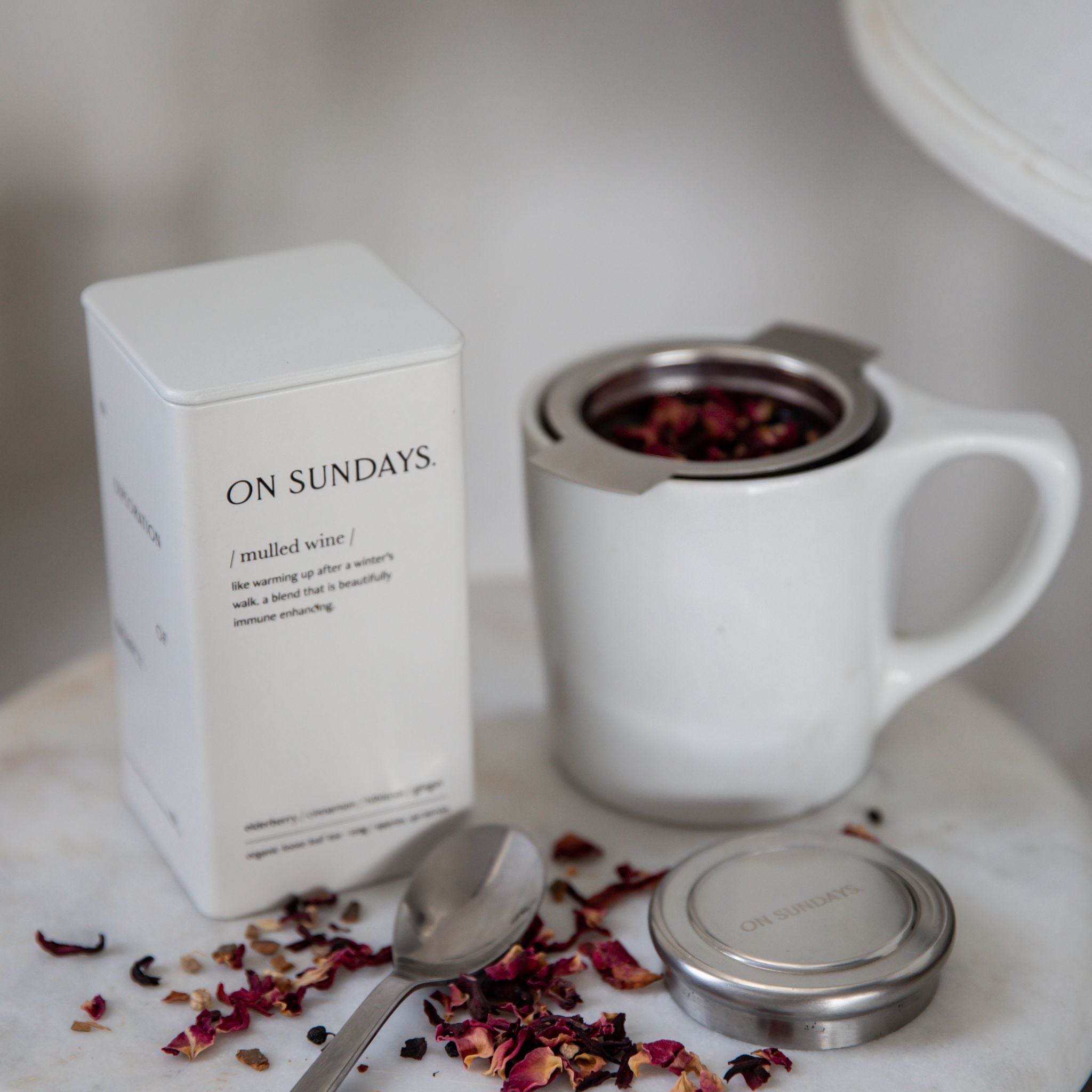 On Sundays Mulled Wine organic loose leaf herbal tea with hibiscus cinnamon ginger and elderberry shown with stainless steel tea infuser mug and white 40 serve storage tin.