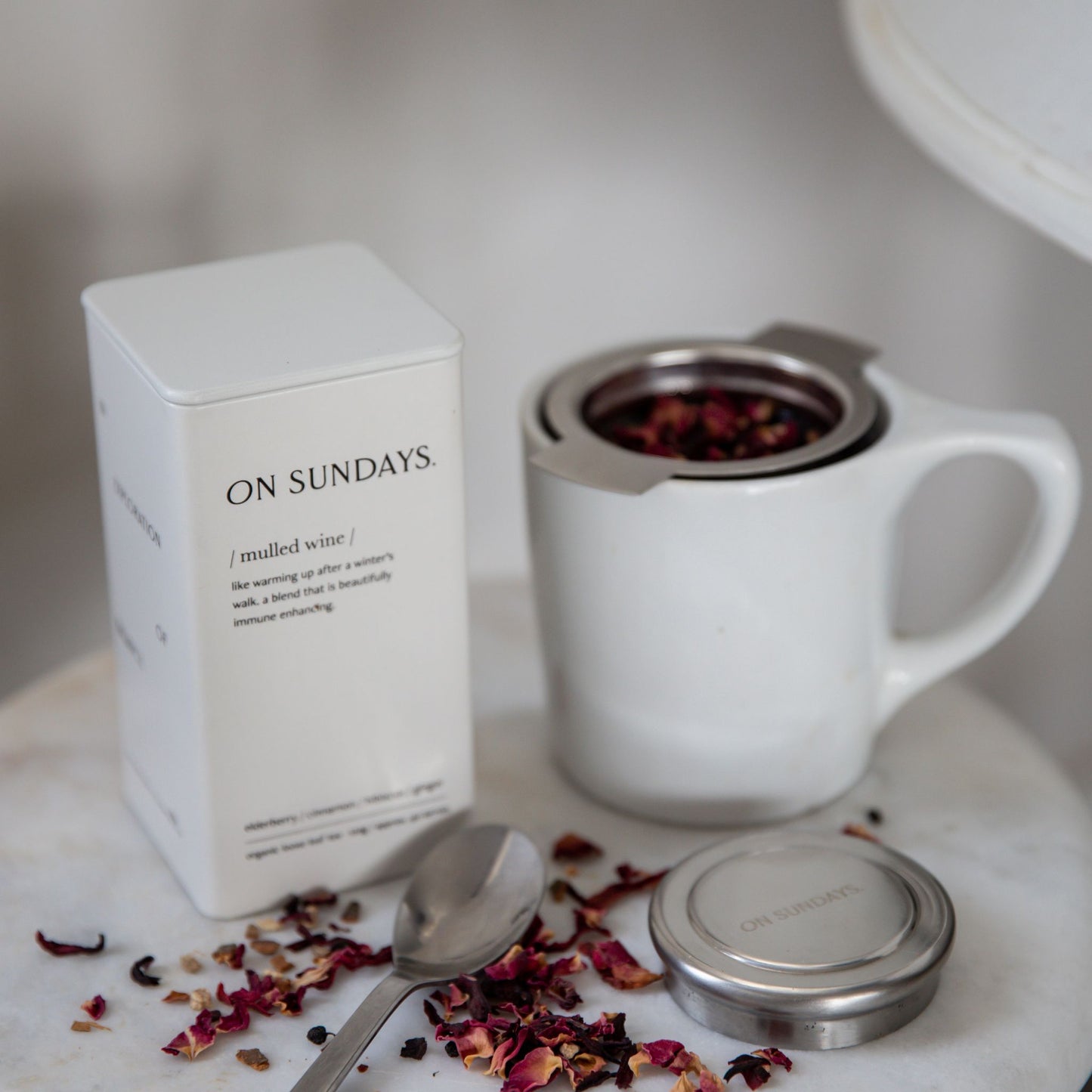 On Sundays Mulled Wine organic loose leaf herbal tea with hibiscus cinnamon ginger and elderberry shown with stainless steel tea infuser mug and white 40 serve storage tin.