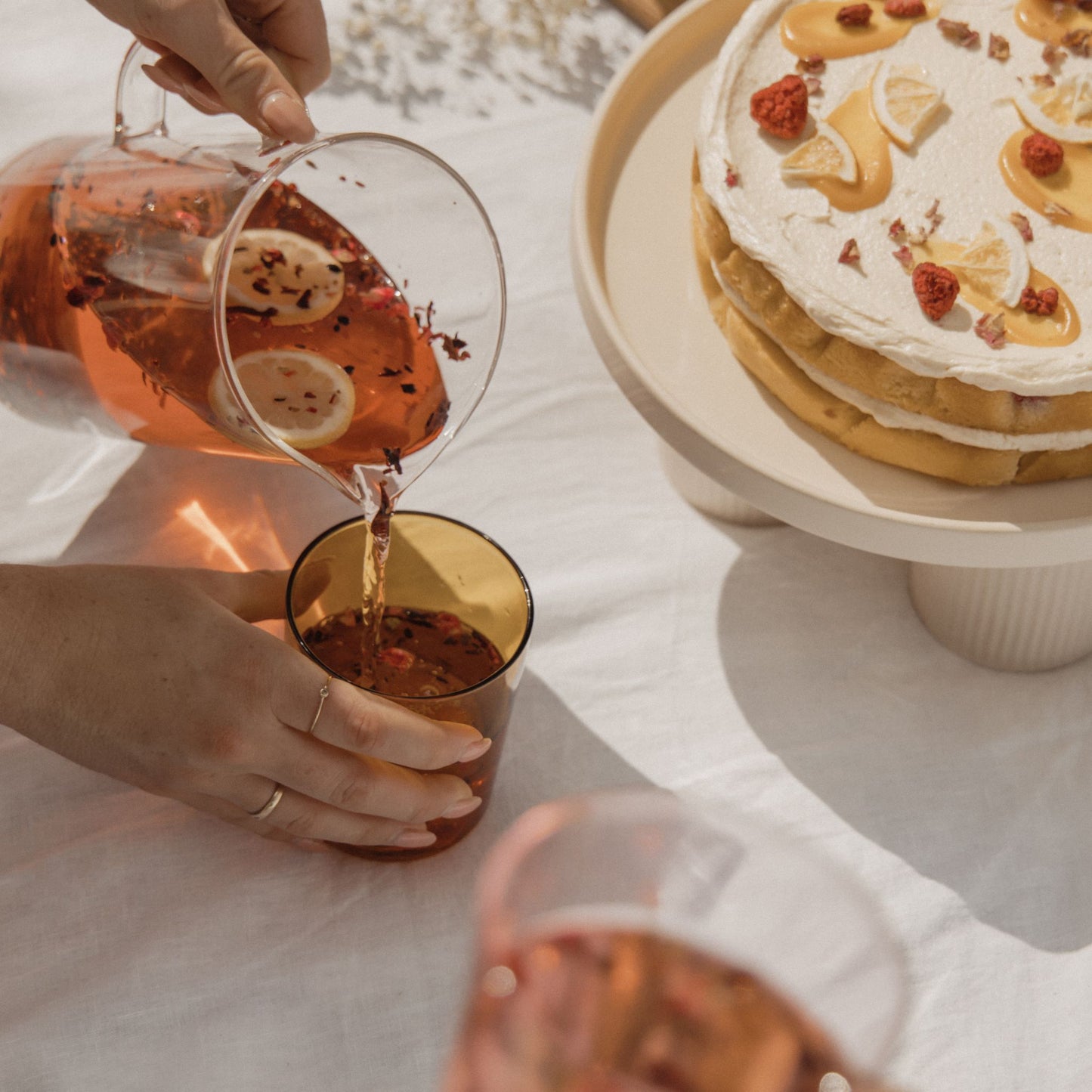 On Sundays Mulled Wine organic loose leaf herbal tea being poured with lemon slices and hibiscus into glass beside layered cake for afternoon tea setting.
