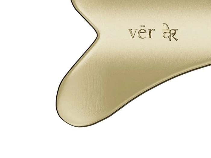 Close-up of vēr वेर Kansa Gua Sha showing engraved brand name on smoothly curved golden Kansa metal surface