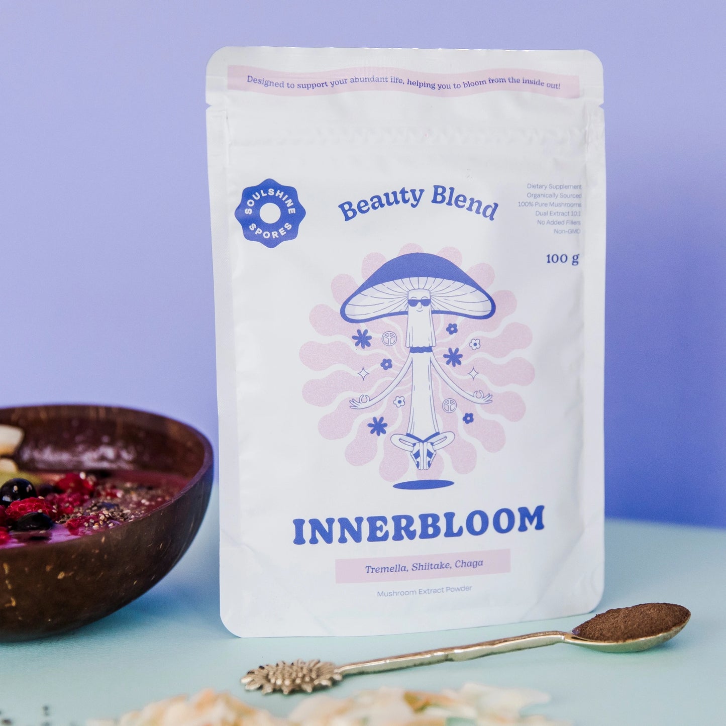 A pouch of Soulshine Spores InnerBloom Beauty Blend, a 100% organic medicinal mushroom powder featuring Tremella, Shiitake, and Chaga with a smoothie bowl and a spoon of  the mushroom powder.