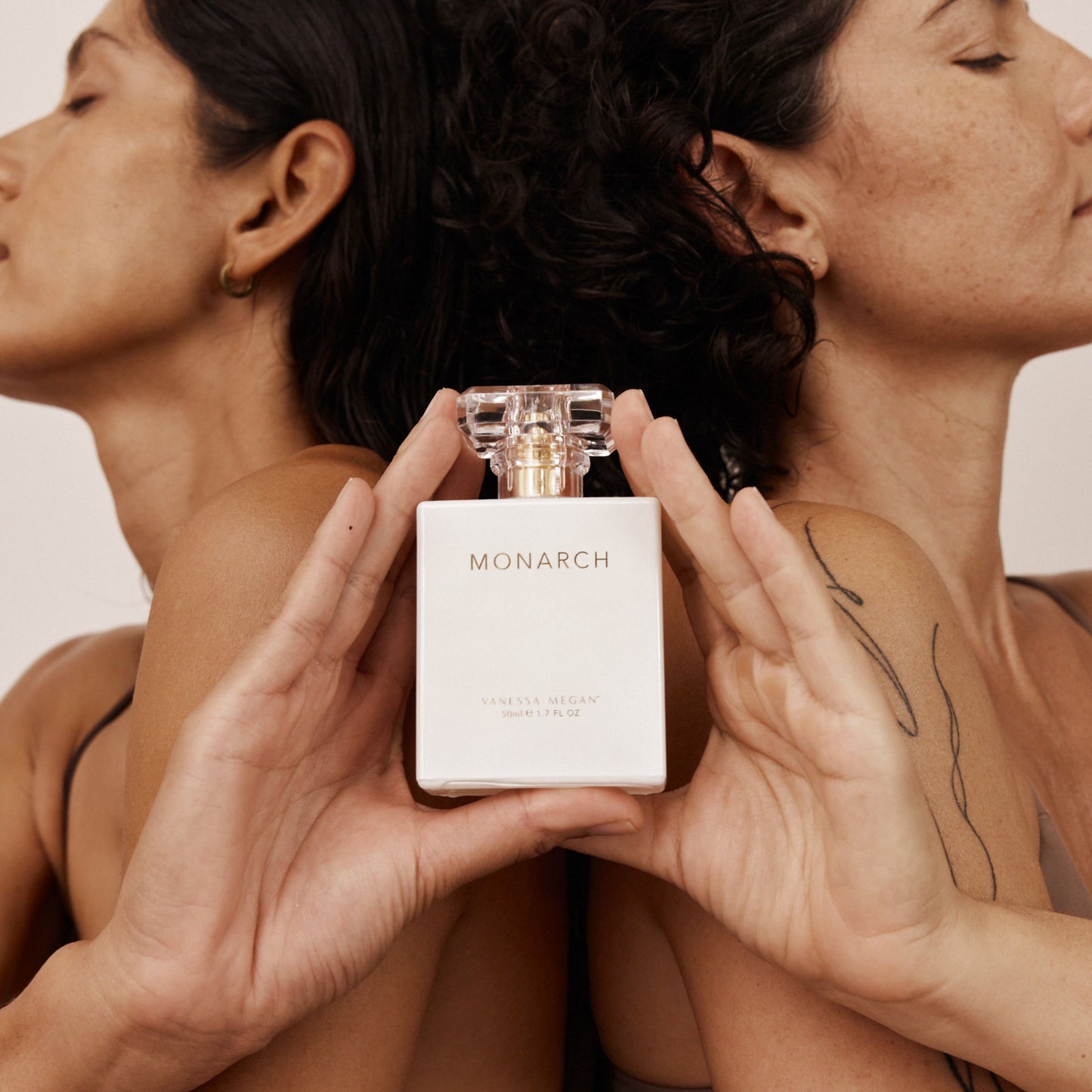Two women posed back to back, peacefully eyes closed, holding a bottle of Vanessa Megan Monarch natural perfume.
