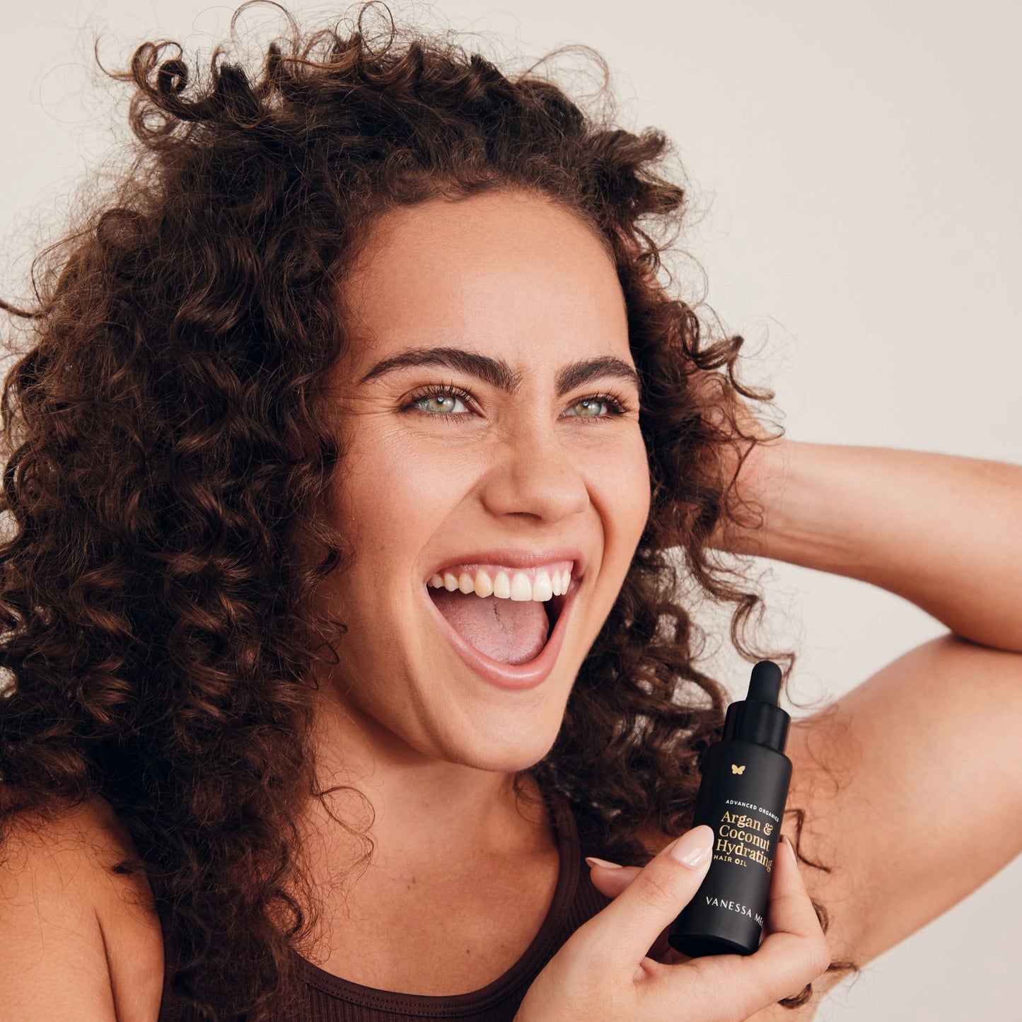 woman with curly hair holding Vanessa Megan Argan and Coconut Hydrating Hair Oil — 100% natural, lightweight hair oil for frizz control and shine