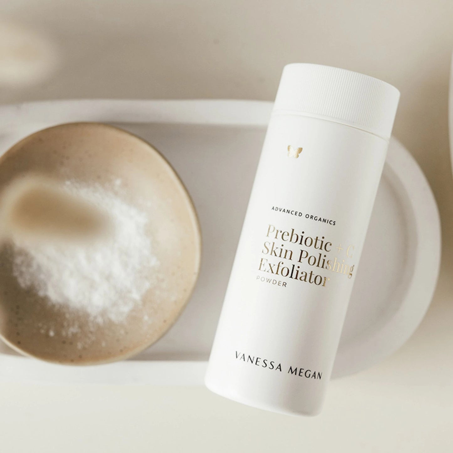 Flatlay of Vanessa Megan Prebiotic + C Exfoliating Powder and ceramic dish of powder on a soft-toned tray.