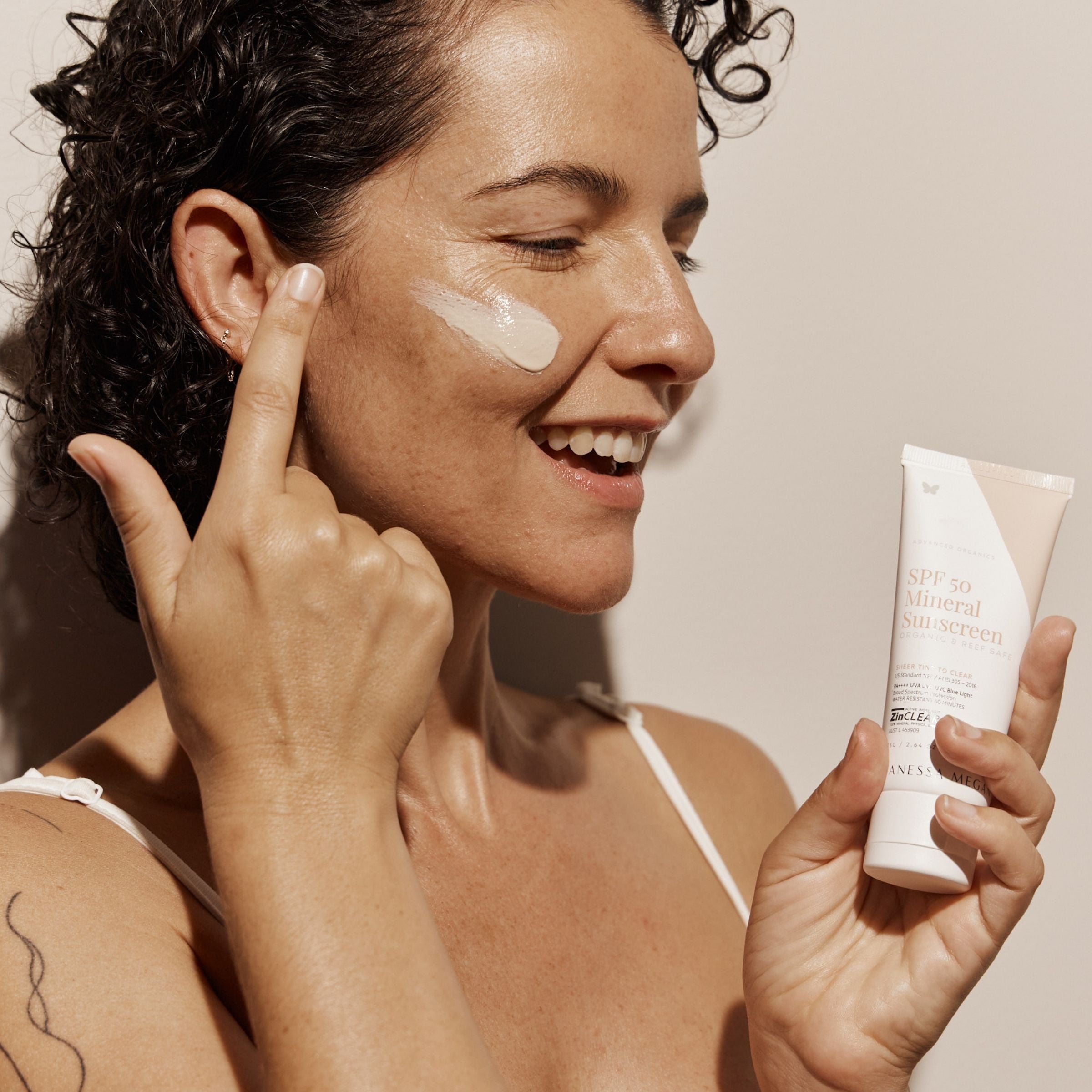 Smiling woman applying Vanessa Megan SPF 50 Mineral Sunscreen, a reef-safe natural sun protection for daily face and body skincare.
