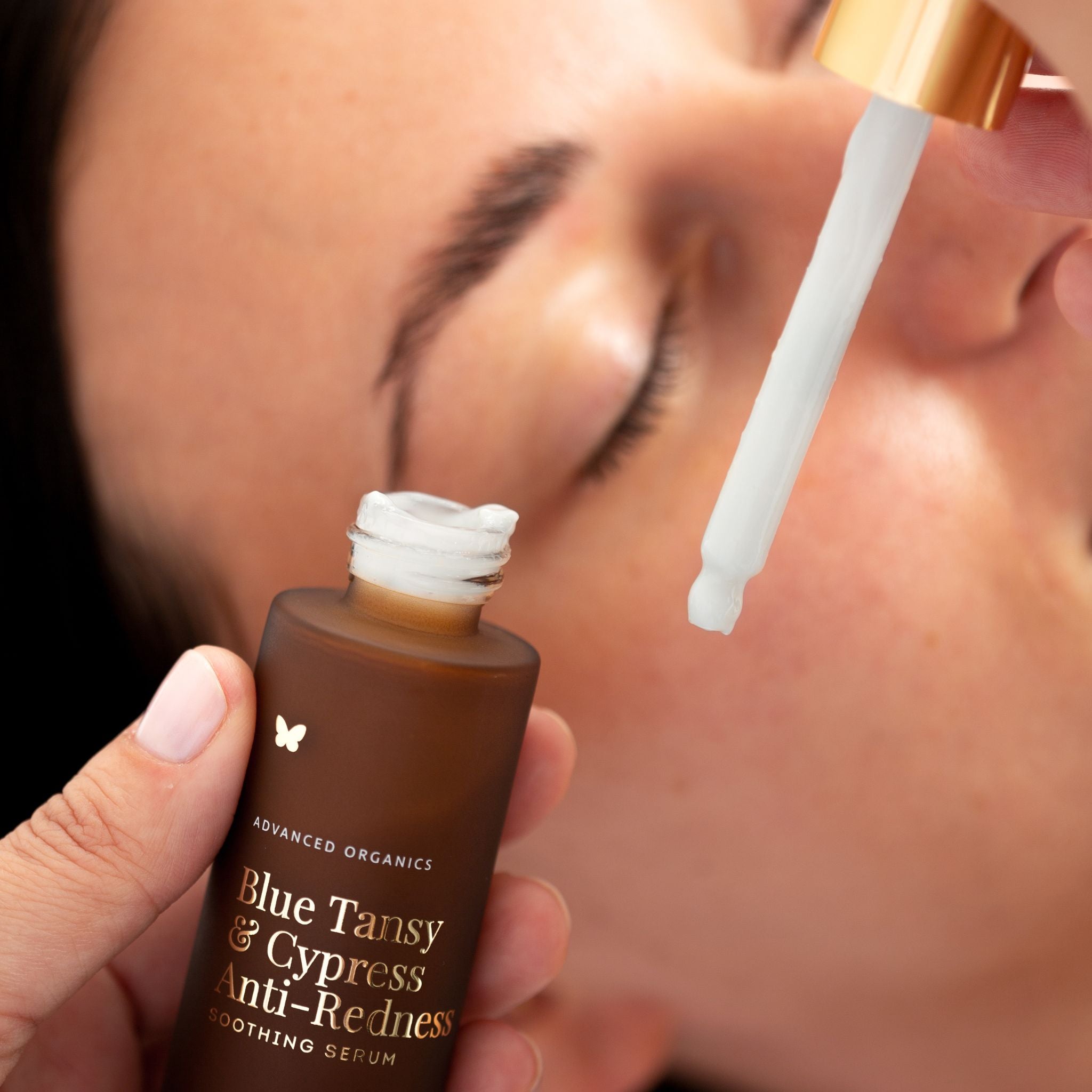 Hand holding Vanessa Megan Blue Tansy and Cypress Anti Redness Soothing Serum bottle close to face with dropper lifted, model with eyes closed in background showing calming sensitive skin skincare application.