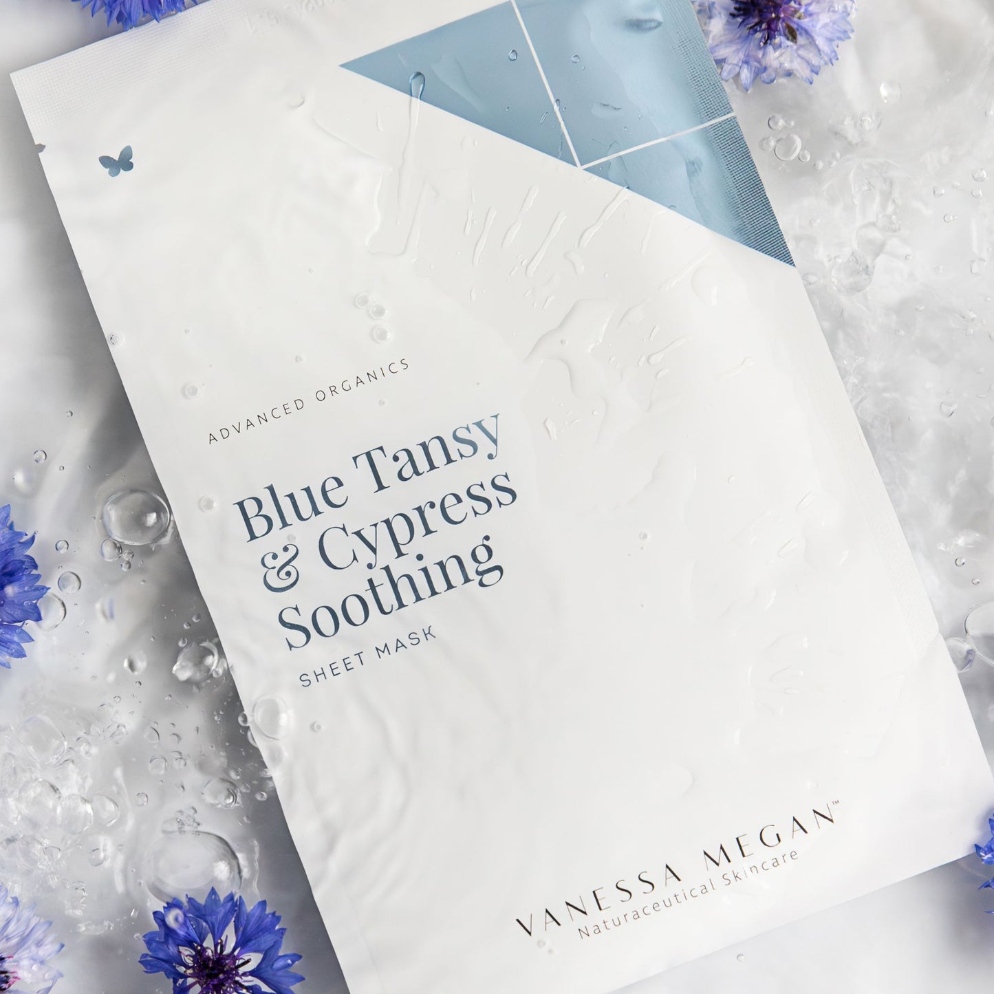 nessa Megan Blue Tansy and Cypress Soothing Sheet Mask single pouch on water textured background surrounded by blue tansy flowers, hydrating calming face mask for sensitive skin.