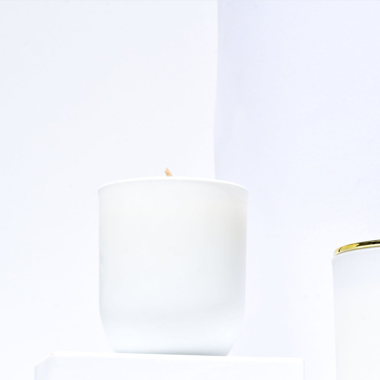 Vanessa Megan Monarch 100% Natural Soy Wax Candle back view in white glass jar with visible cotton wick, and a second candle with gold lid partially shown in the foreground.