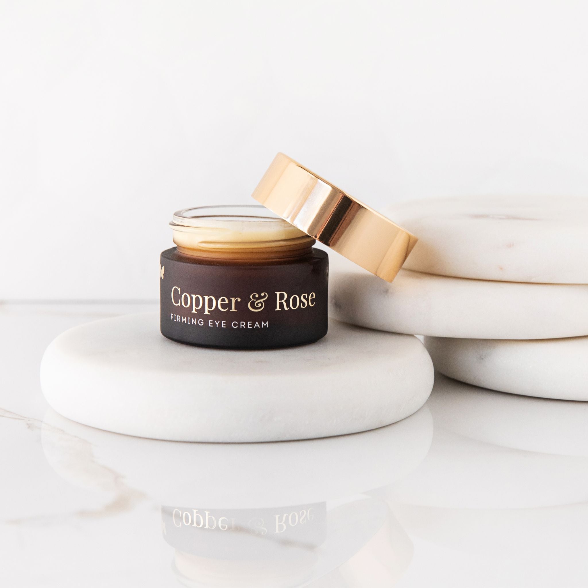 Vanessa Megan Copper and Rose Firming Eye Cream open jar, on natural stone and white background.