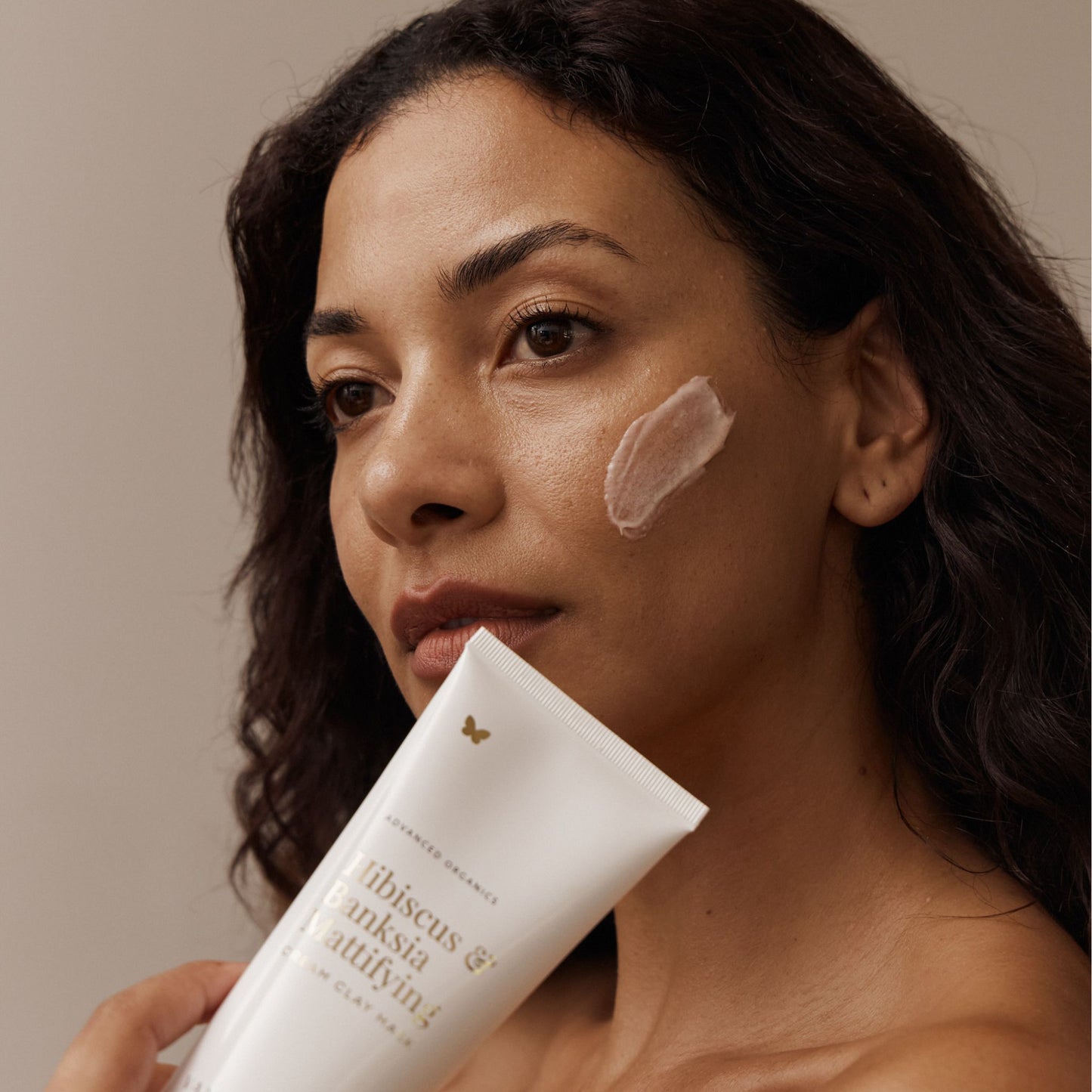 Woman with Vanessa Megan Hibiscus and Banksia Mattifying Cream Clay Face Mask applied to cheek holding the recyclable squeeze tube.