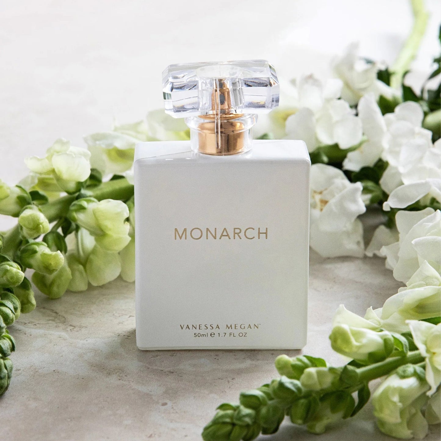 Monarch Perfume placed among fresh white florals on a stone surface.