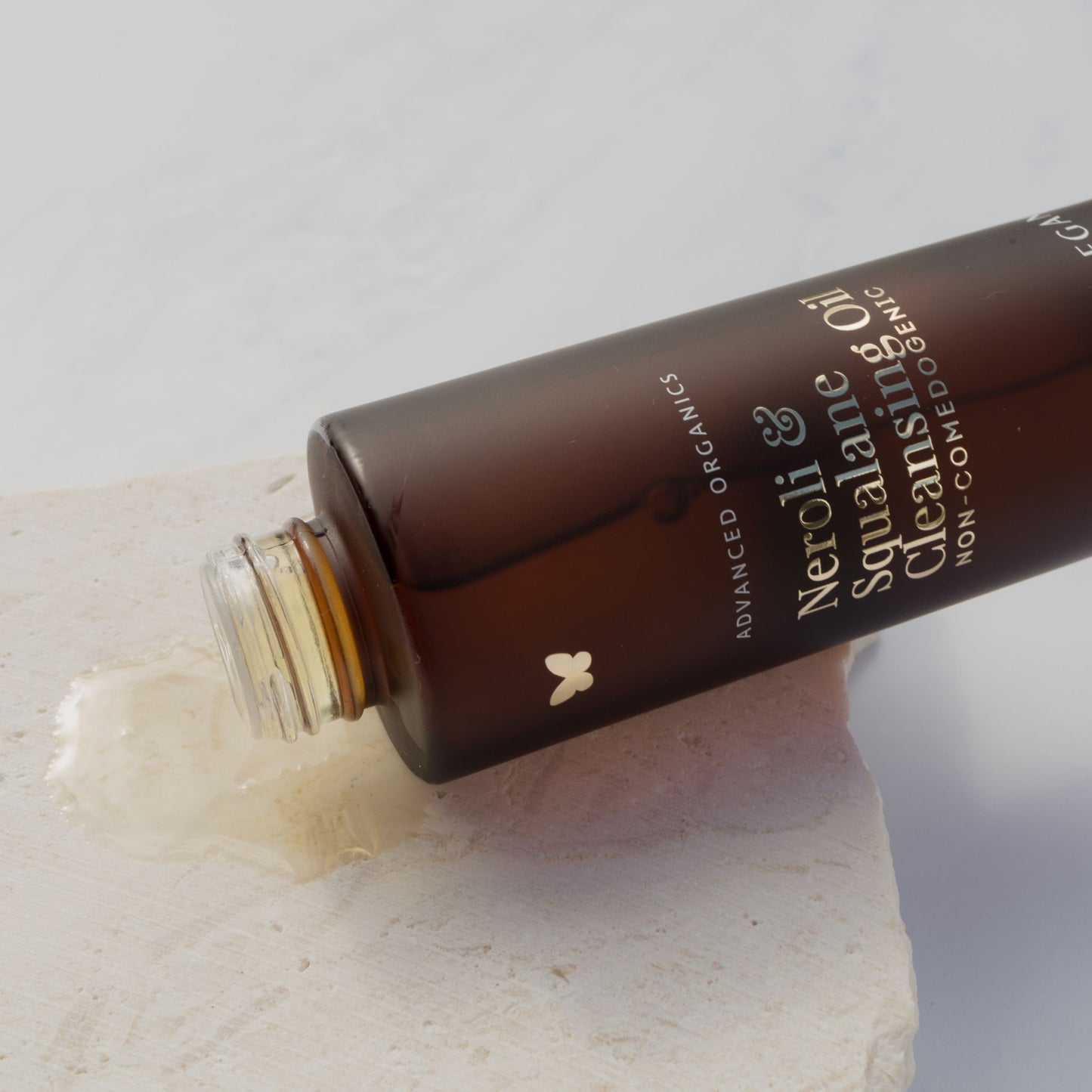 Vanessa Megan Neroli and Squalane Cleansing Oil bottle with spilled oil texture on stone surface.