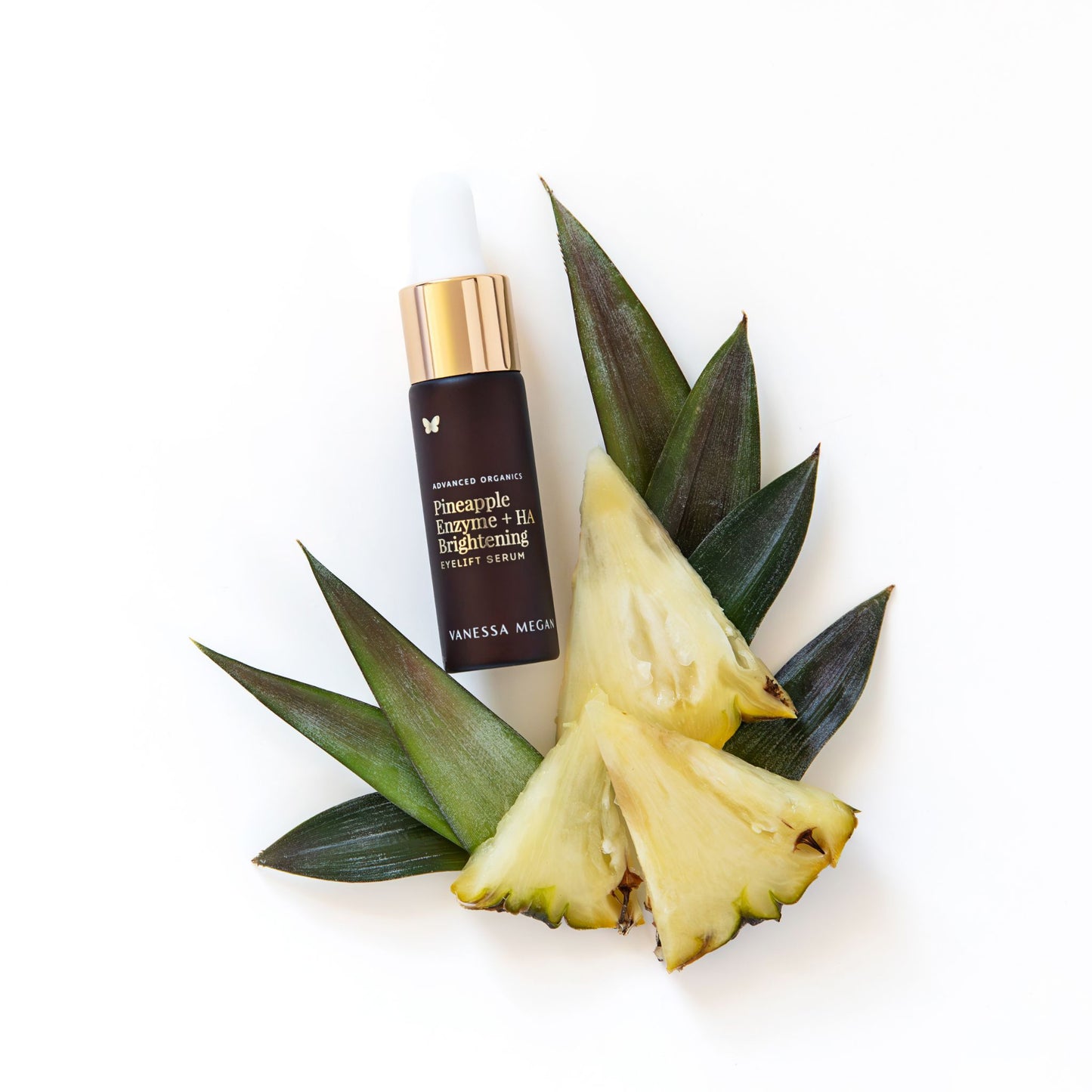 Vanessa Megan Pineapple Enzyme + HA Brightening Eyelift Serum styled with fresh pineapple slices and green leaves on white background.