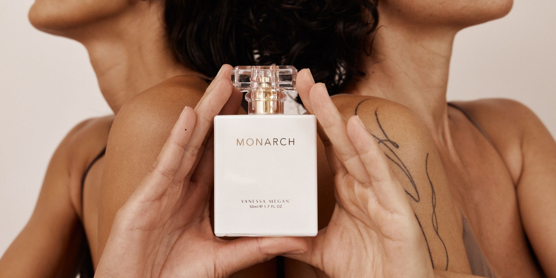 Two women hold a bottle of Vanessa Megan Monarch 100% Natural Perfume between them. Discover and shop this award-winning natural fragrance at Intentionally Natural NZ.