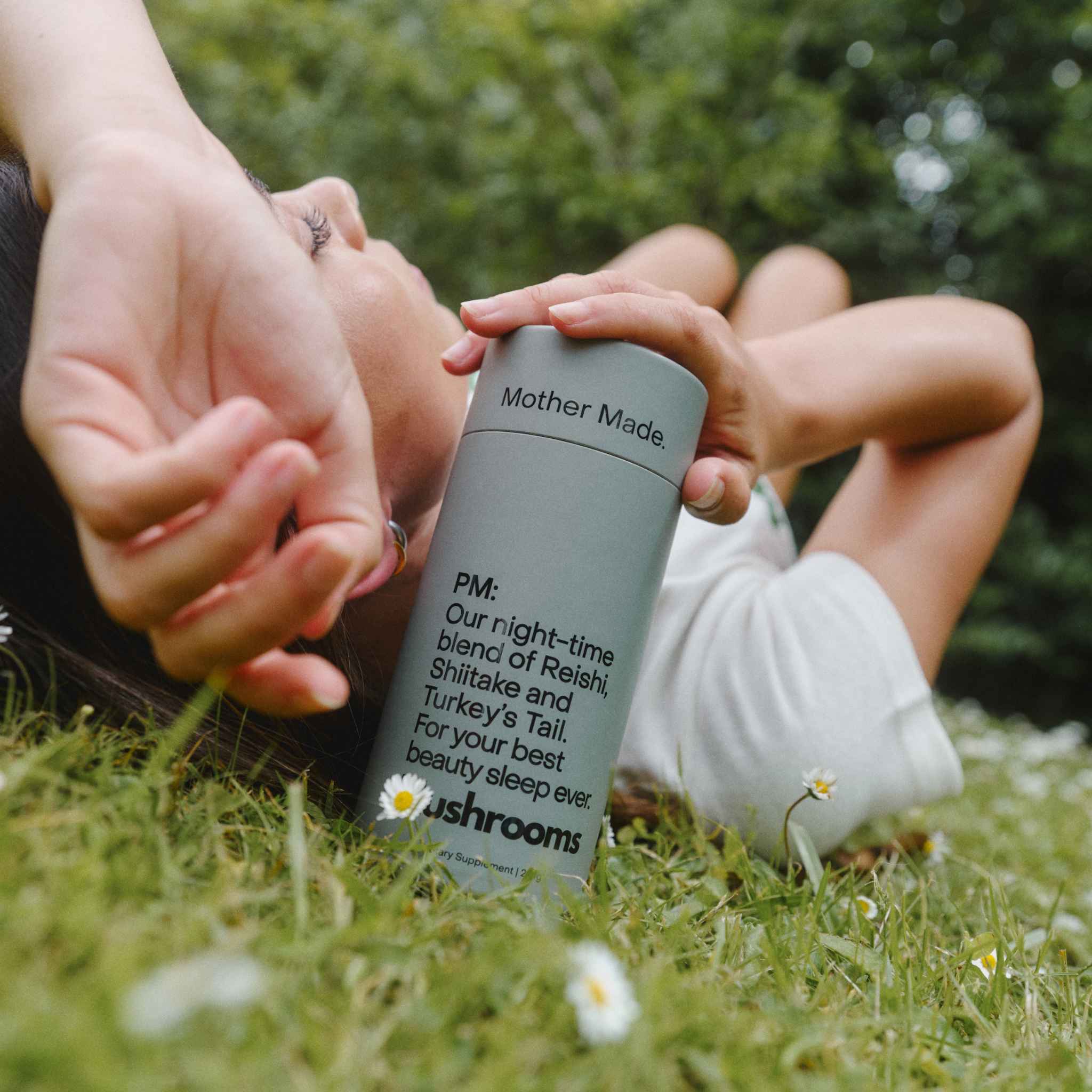 Women laying on grass holding a canister of the Mother Made PM Blend Reishi, Shiitake and Turkey’s Tail mushroom powder.