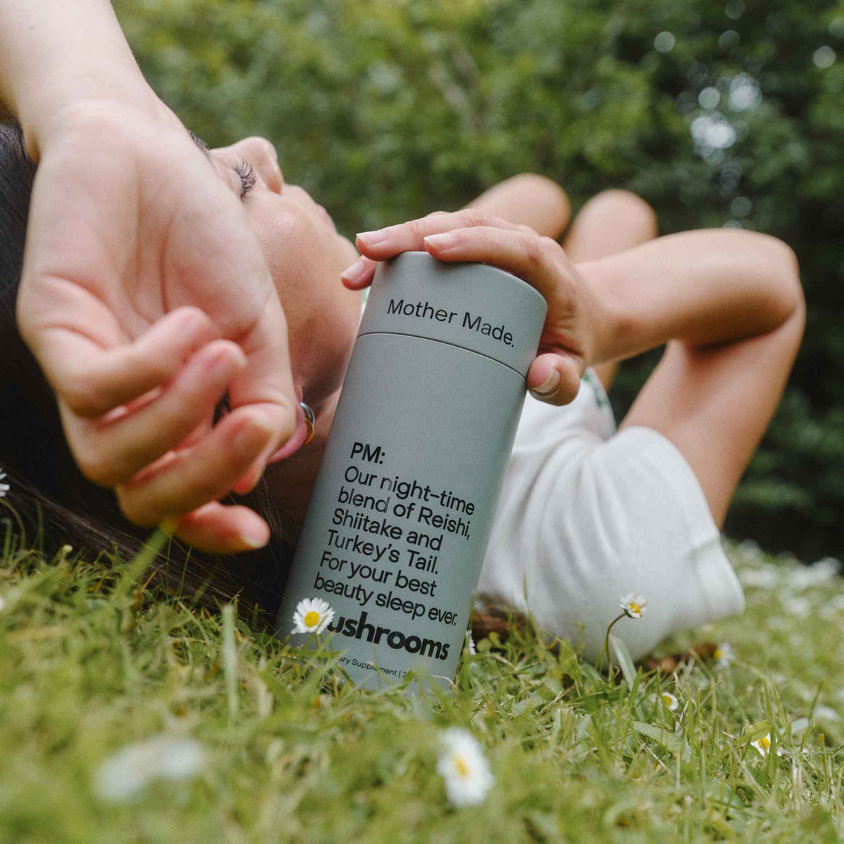 Women laying on grass holding a canister of the Mother Made PM Blend Reishi, Shiitake and Turkey’s Tail mushroom powder.