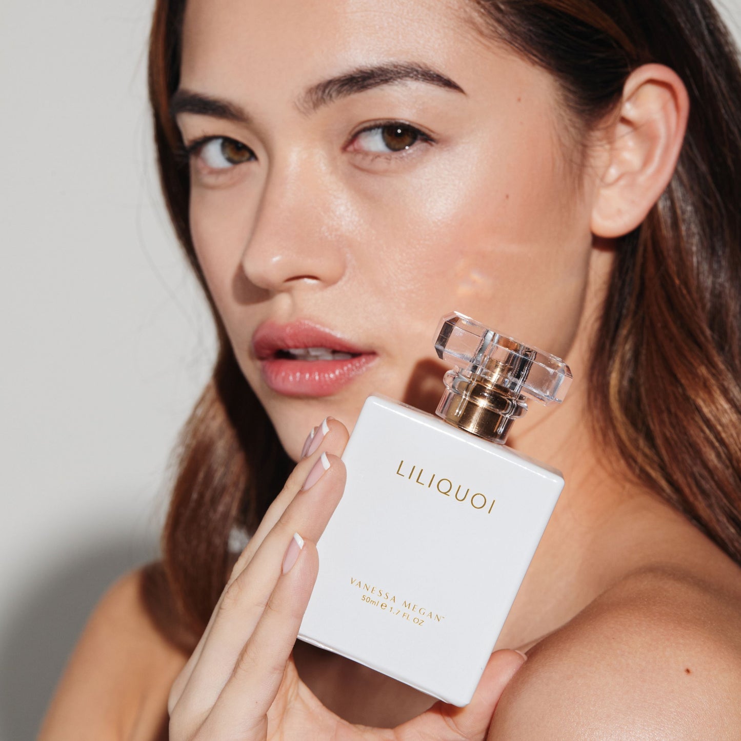 Close-up of woman with glowing skin holding Vanessa Megan Liliquoi 100% Natural Perfume 50ml, showcasing the luxury white and gold bottle. Discover and shop this award-winning natural fragrance at New Zealand’s top destination for Vanessa Megan skincare and perfume.